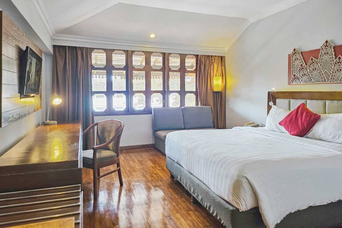 A hotel room with a bed, a desk, a chair, and a window with curtains.