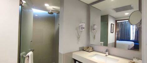Un bagno moderno con cabina doccia in vetro, doppio lavabo e un grande specchio che riflette una camera da letto.