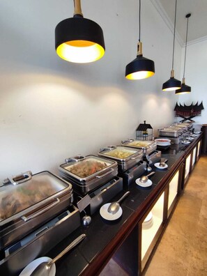 A buffet setup with multiple food stations, each with covered dishes and serving utensils. - Monopoli Hotel Bukittinggi (Bukittinggi)