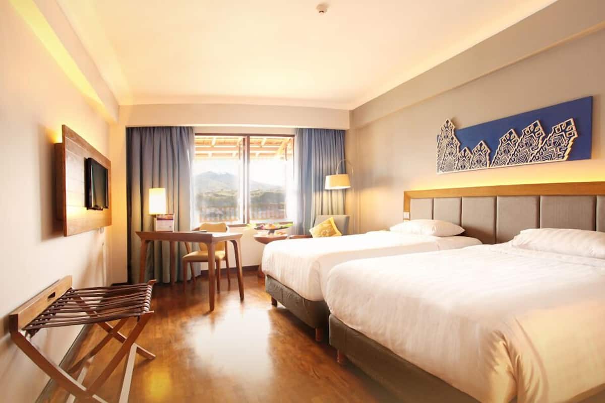 A hotel room with two beds, a desk, a chair, and a view of the outdoors.