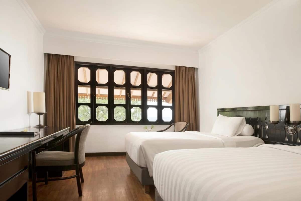 A hotel room with a bed, a desk, a chair, and a window with curtains.