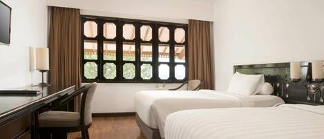 Una habitación de hotel con cama, escritorio, silla y ventana con cortinas.