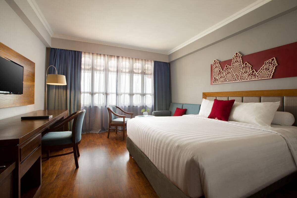A hotel room with a large bed, a desk with a chair, a television, and a decorative wall piece.