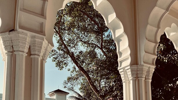 An outdoor seating area with white columns, blue cushioned chairs, and umbrellas. - Monopoli Hotel Bukittinggi (Bukittinggi)