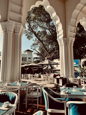 Un área de estar al aire libre con columnas blancas, sillas acolchadas azules y sombrillas.