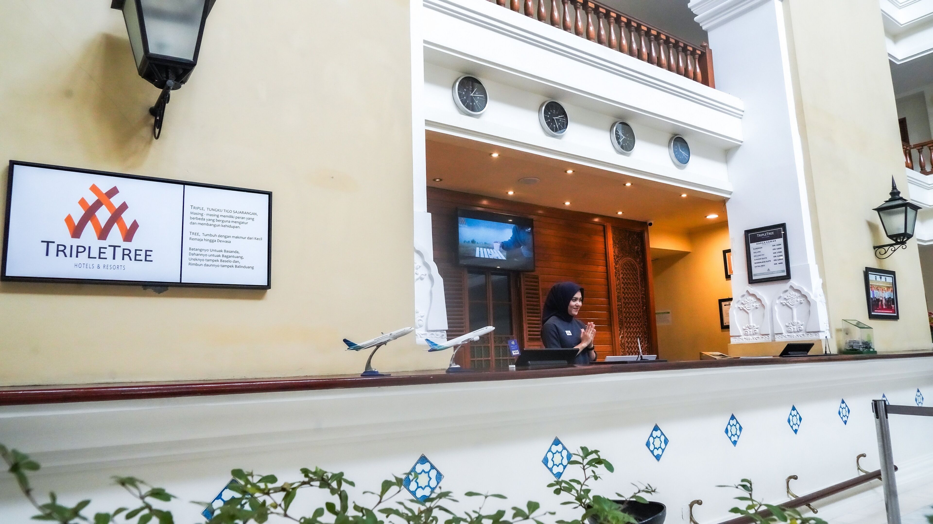 A reception area with a sign for TripleTree Hotels & Resorts, a television screen, and a decorative wall with a clock.