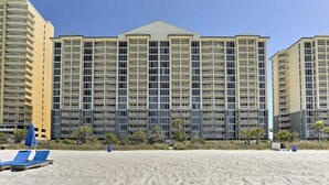 Ein Strandhotel mit mehreren Hochhäusern, einem Sandstrand und blauen Liegestühlen.