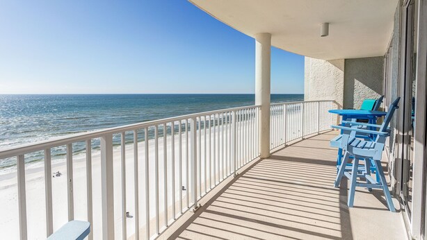 Ein Balkon mit Blick auf das Meer, einem weißen Geländer und blauen Stühlen.