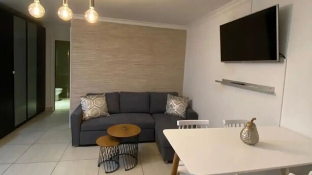 Una sala de estar moderna con un sofá gris, una mesa de centro y un comedor con una mesa y sillas blancas.