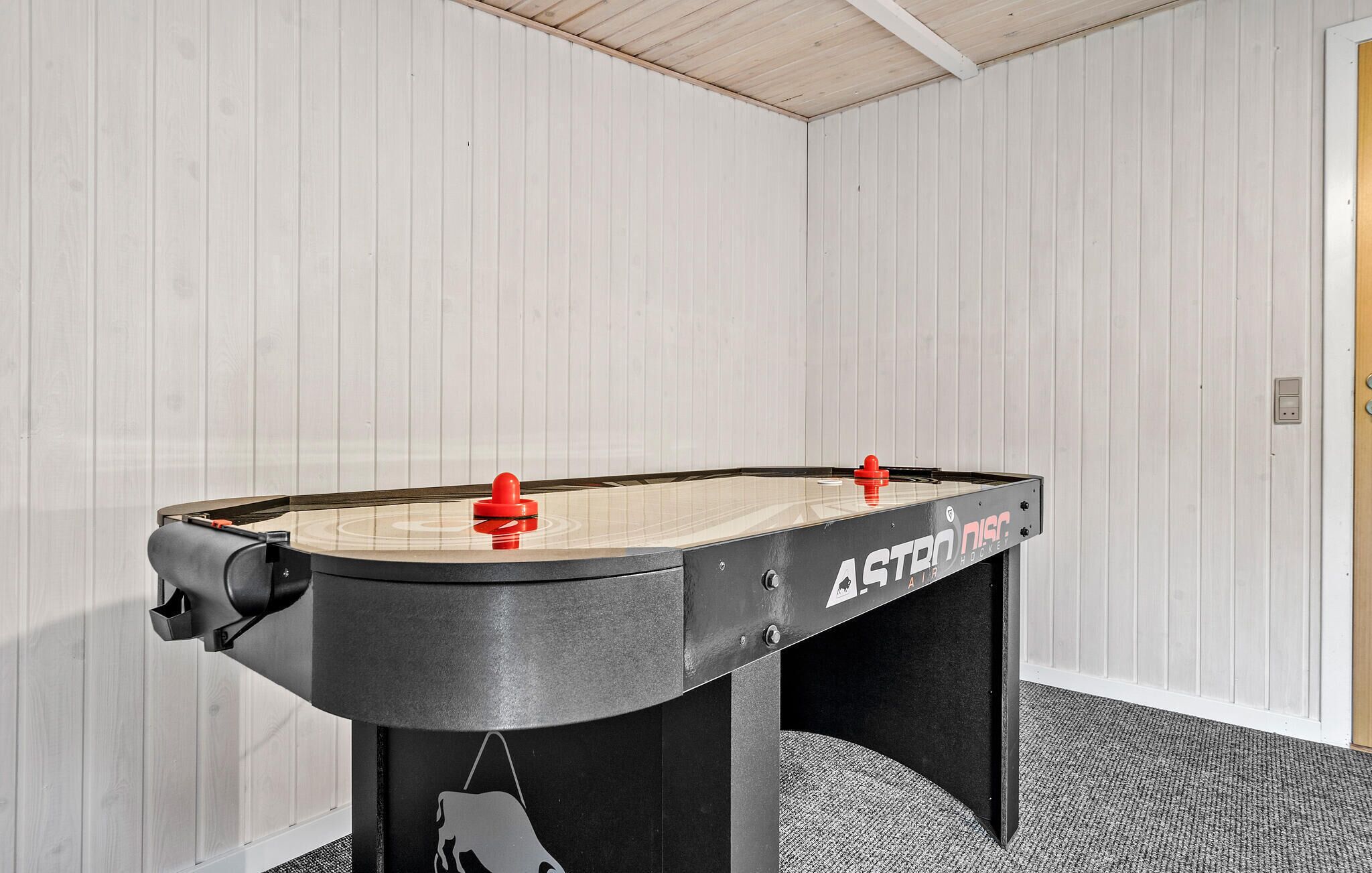 A foosball table in a room with white paneled walls and a carpeted floor.