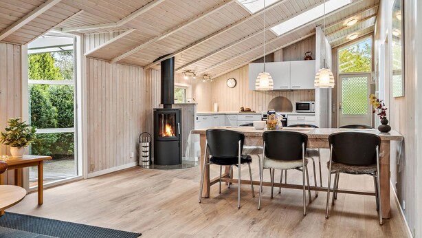 Une cuisine moderne dotée d’un îlot central, de poutres en bois au plafond et de grandes fenêtres.