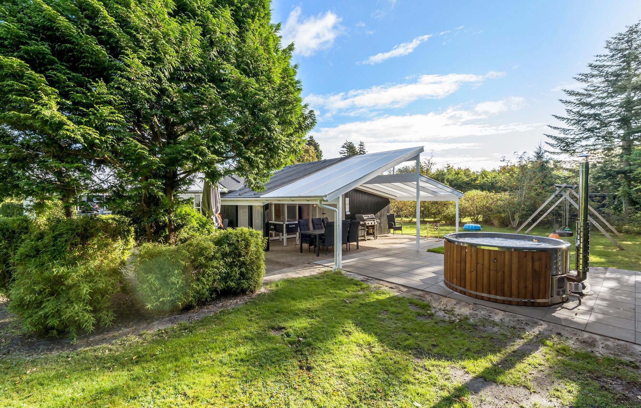 Un patio extérieur couvert, équipé d’un barbecue et d’un espace salon, entouré d’une végétation luxuriante et agrémenté d’un jacuzzi.
