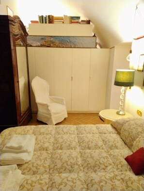 Een slaapkamer met een bed, een stoel, een lamp en een kledingkast.
