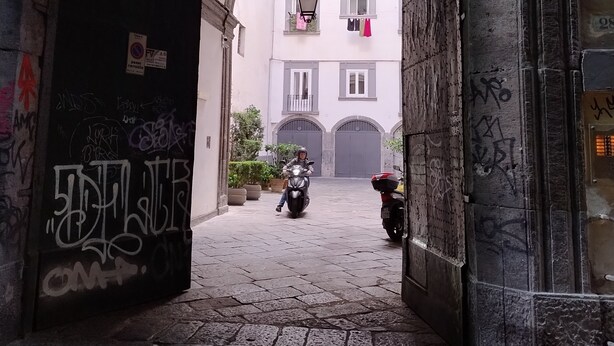 An urban alleyway with a stone archway, a scooter, and a building with balconies and a hanging lantern. - Luxury Apartment in historical 15th century building (Napoli)