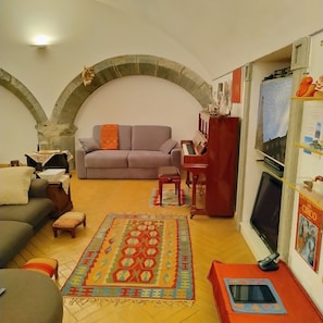 A living room with a sofa, a small table, a piano, and a TV.
