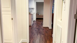Un couloir doté d’un plancher en bois, de murs blancs et d’un coin cuisine à l’arrière-plan.