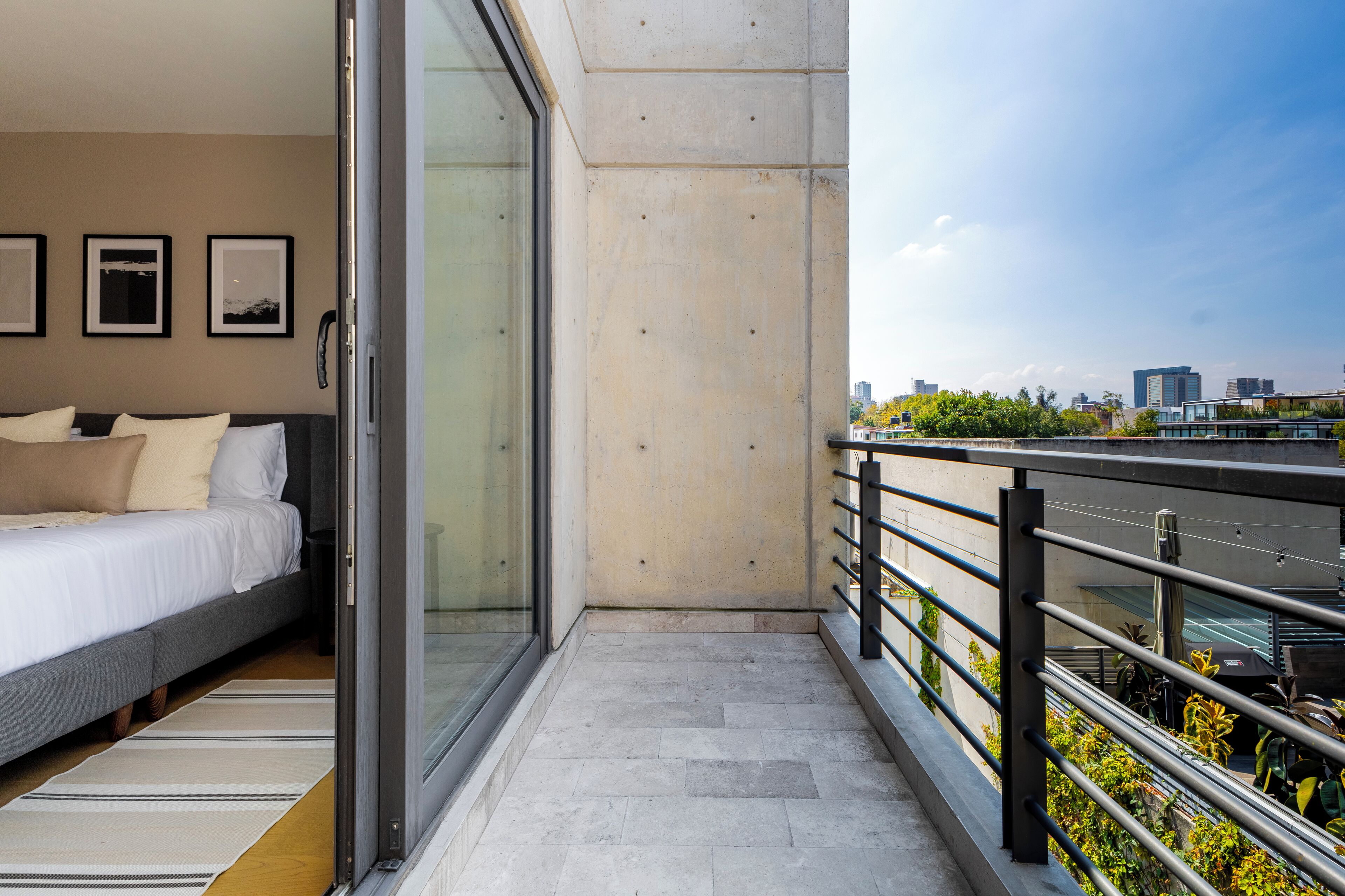 A modern hotel room with a bed, a glass door leading to a balcony, and a city view.