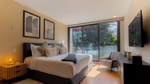 Una camera da letto moderna con un letto grande, una scrivania e una sedia. Si vede una finestra con vista su edifici e alberi.