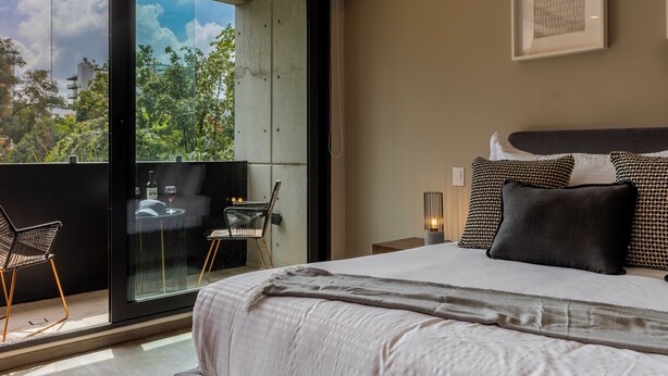 Una camera da letto moderna con un letto grande, un balcone con porta vetrata e vista sul verde.