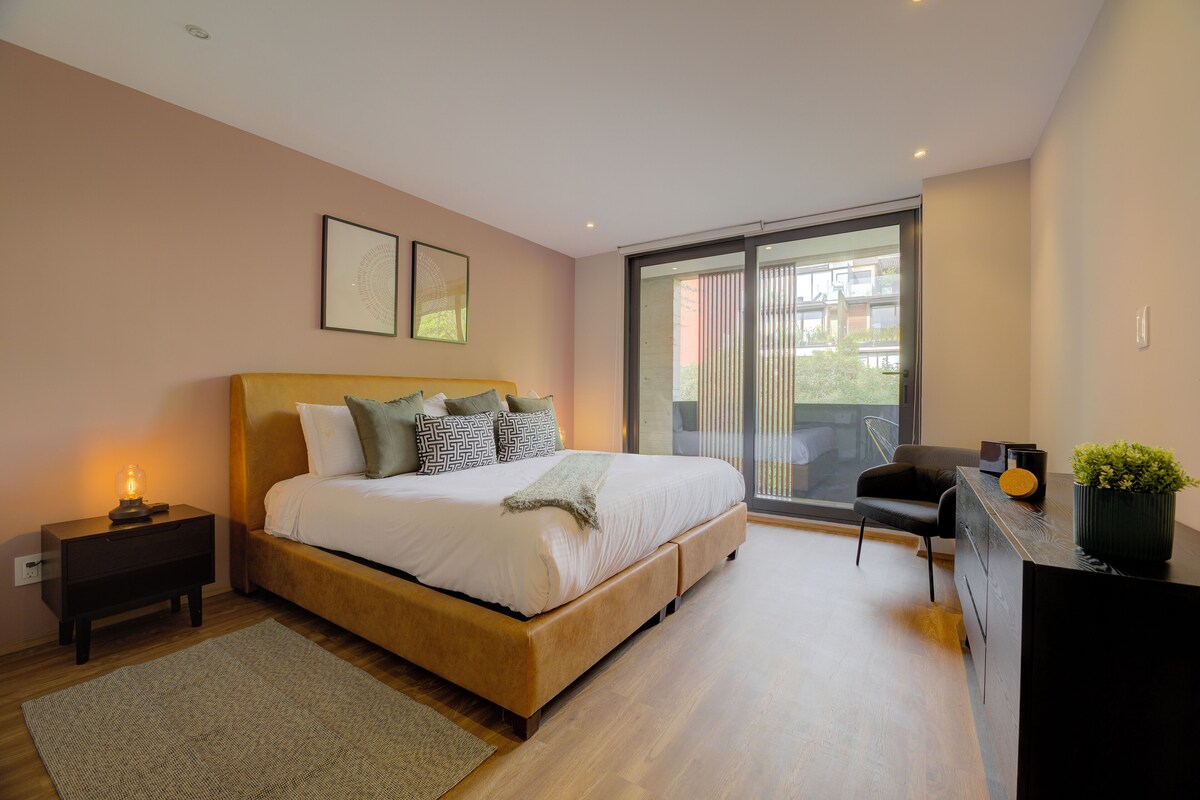 A modern bedroom with a large bed, a nightstand, a desk, and a view of the outdoors.