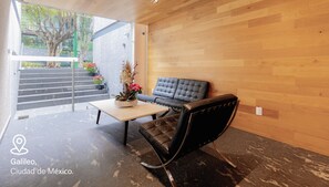 A modern interior with a wooden wall, a black leather sofa, and a glass door leading outside. - Capitalia Galileo Residences (Mexico City)