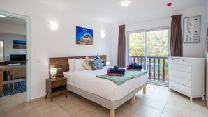 Een slaapkamer met een bed, nachtkastje, lamp en uitzicht op de omgeving door een groot raam.