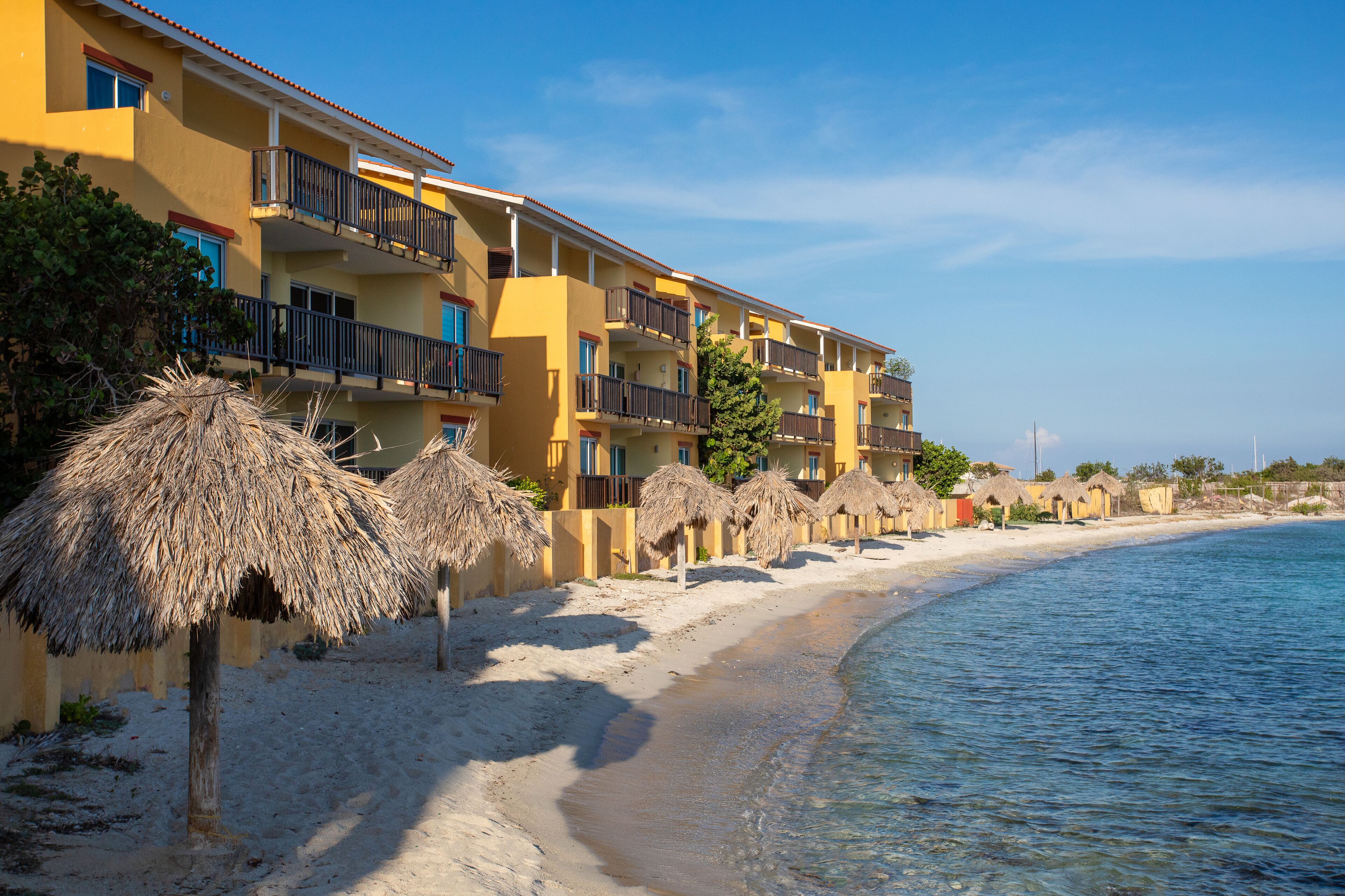 A beachfront hotel with multiple balconies, thatched umbrellas, and a sandy beach.