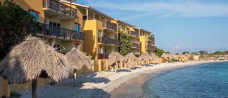 A beachfront hotel with multiple balconies, thatched umbrellas, and a sandy beach.