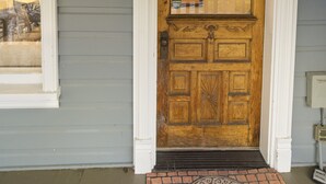 Une porte d’entrée en bois, avec le numéro « 508 » au-dessus, un petit luminaire placé juste au-dessus de la porte, et un paillasson à motifs de briques devant.