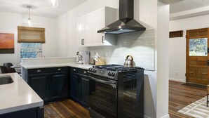 Une cuisine moderne avec des meubles de couleur sombre, un îlot central et une cuisinière. On y trouve des luminaires suspendus et une grande fenêtre.