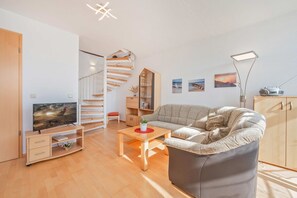 A modern living room with a sofa, a TV, a wooden staircase, and a bookshelf. - Am Strauchelfeld 5 App. 7 - Ferienwohnung Am Strauchelfeld 5 App. 7 (Koserow)