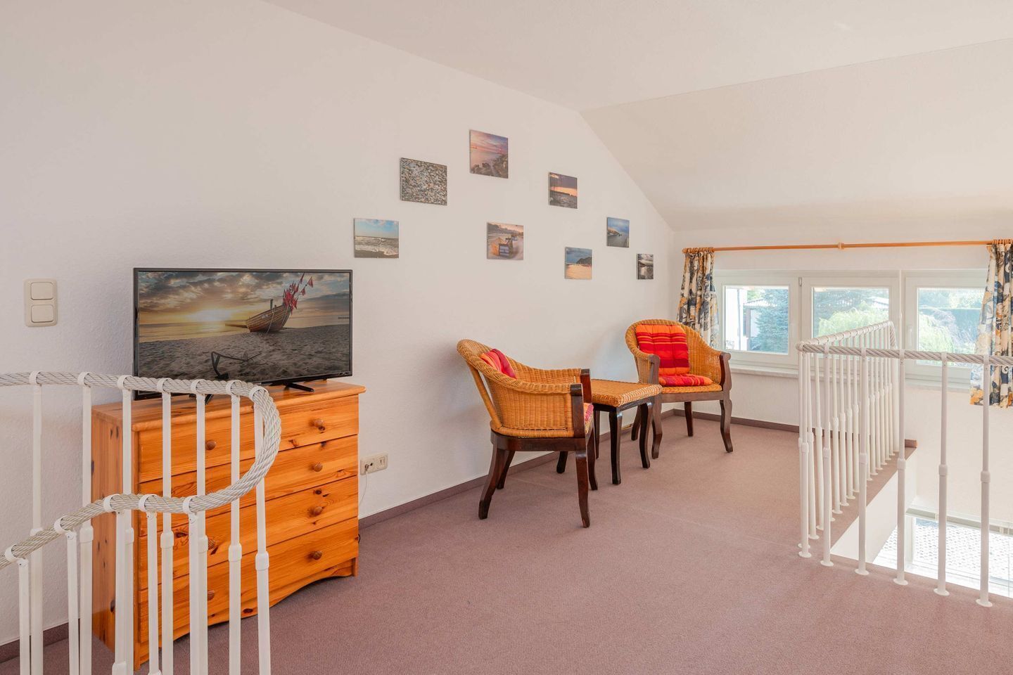 Een kamer met een televisie, een houten dressoir, rieten stoelen en uitzicht op het omliggende landschap door een raam.