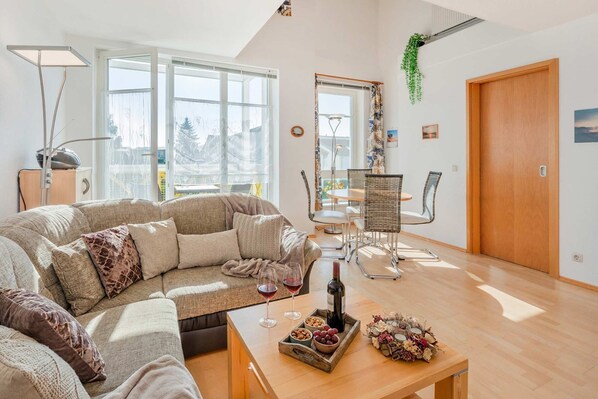A modern living room with a sectional sofa, a dining table with chairs, a wine bottle, and a tray of snacks.