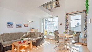 Moderni olohuone, jossa on sohva, sohvapöytä ja ruokailutila tuoleineen. Huoneesta johtaa portaat ylemmälle tasolle.