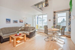 Un salon moderne avec un canapé, une table basse et un coin repas avec des chaises. Un escalier mène à un niveau supérieur.