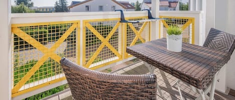 A balcony with wicker furniture, a yellow safety gate, and a potted plant.