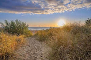 Un sentier sablonneux qui mène à une plage d’où l’on peut admirer l’océan et le coucher du soleil.
