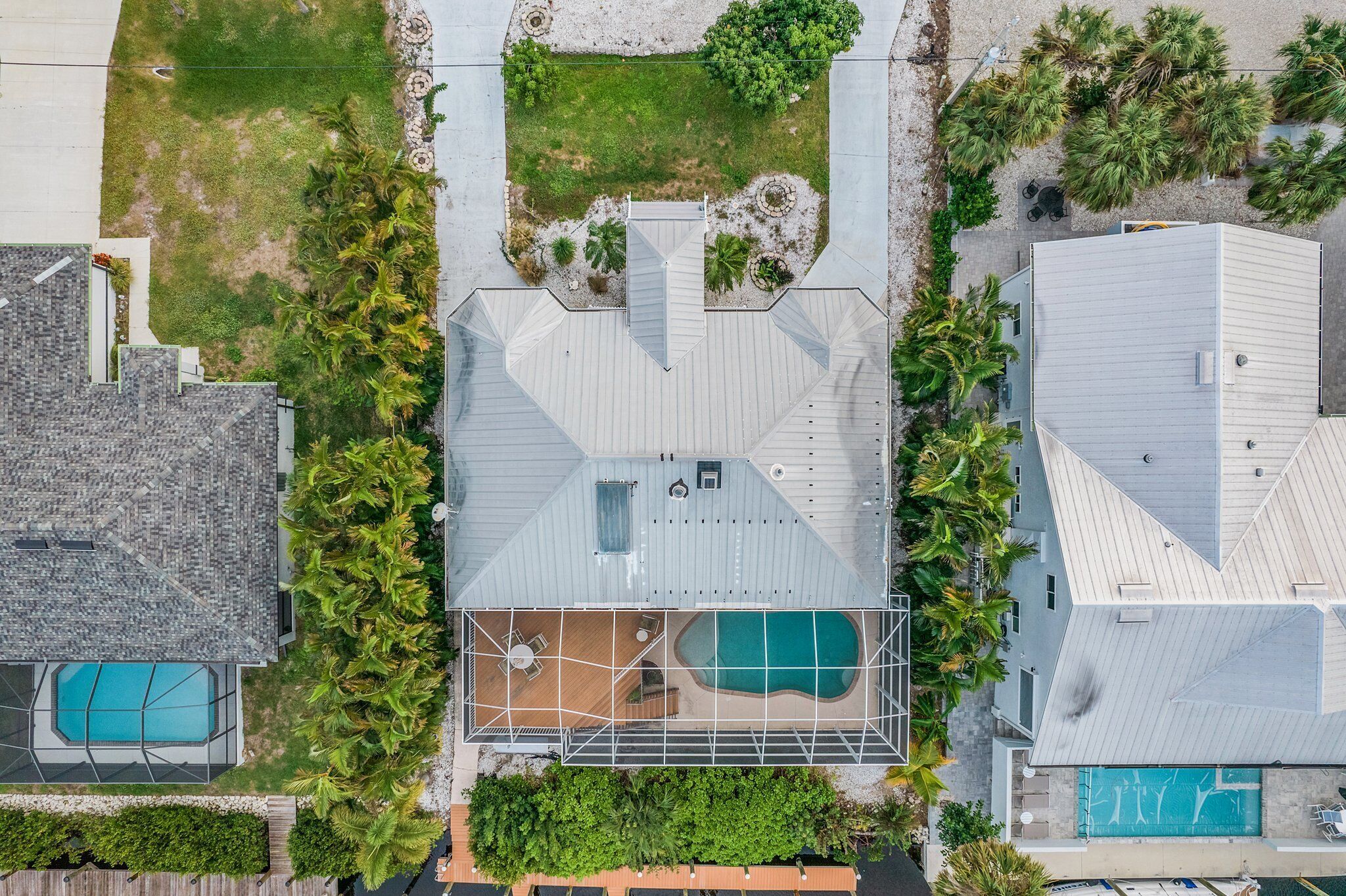 An aerial view of a residential property with two swimming pools, a covered patio area, and surrounding greenery.