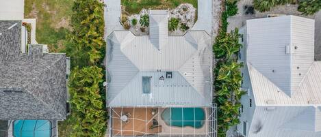 An aerial view of a residential property with two swimming pools, a covered patio area, and surrounding greenery.