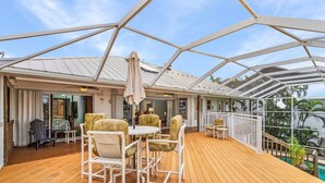 A covered outdoor deck with a wooden floor, white metal railing, and a table with chairs. - 3/2 Pool Home in St. James, Gorgeous Views! (Saint James City)