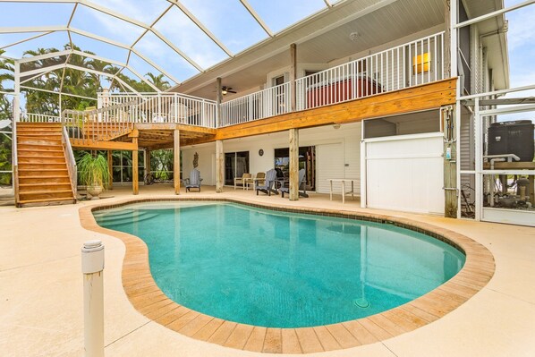 A swimming pool with a wooden deck and a covered upper level with a balcony.