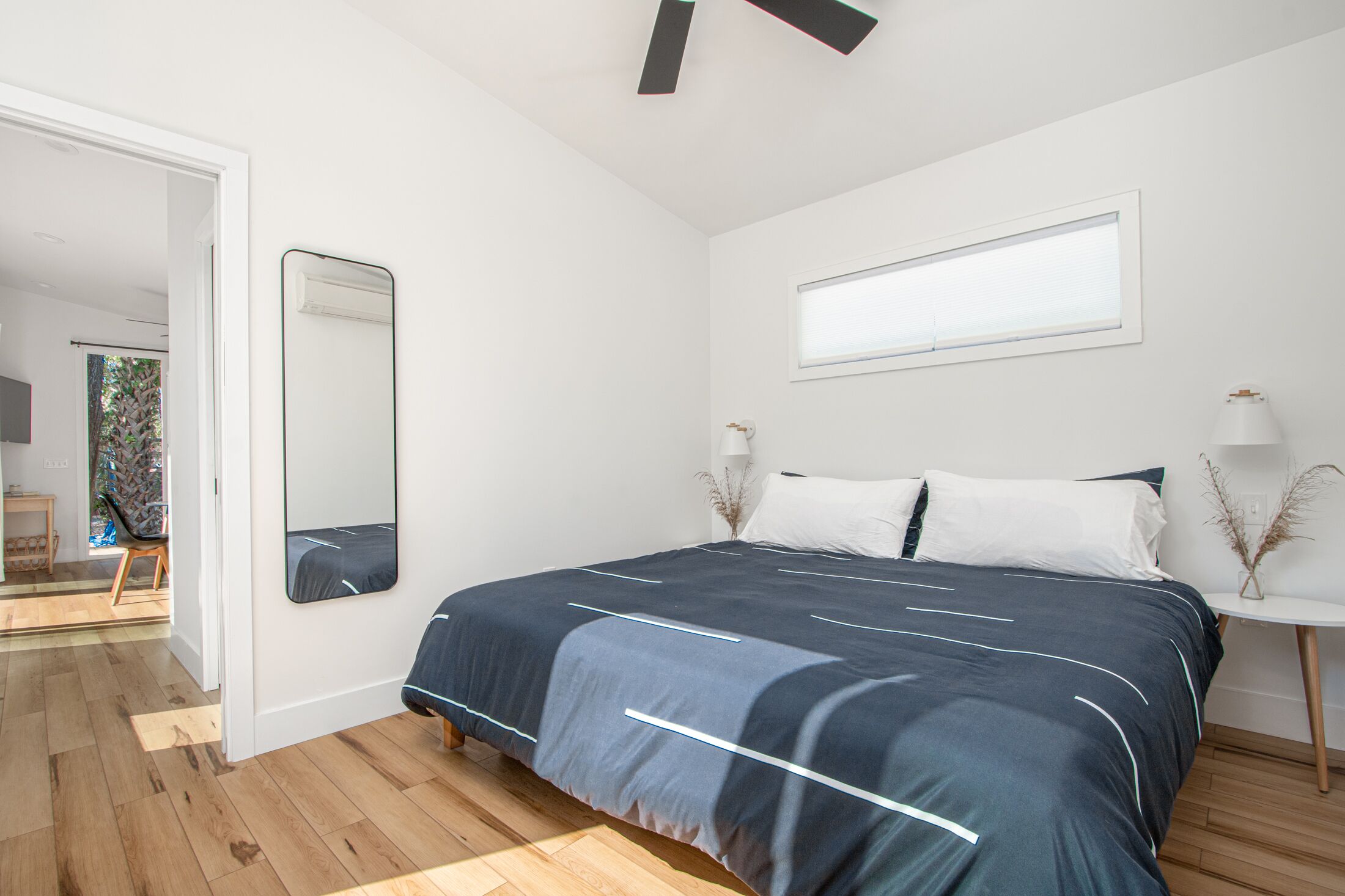 Een slaapkamer met een groot bed, een spiegel, een raam en een klein tafeltje met een lamp.