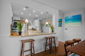 A modern kitchen with a central island, pendant lighting, and wooden stools.