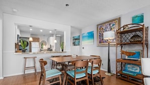 Un comedor con una mesa y sillas de madera, un tapete de cuero de vaca y una estantería con objetos decorativos.