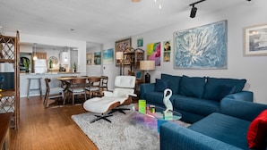 A modern living room with a blue sofa, a white chair, and a dining area with wooden furniture. - La Mirage Condo 305 Beachfront Resort Condominiums with Private Boardwalk (Port Aransas)
