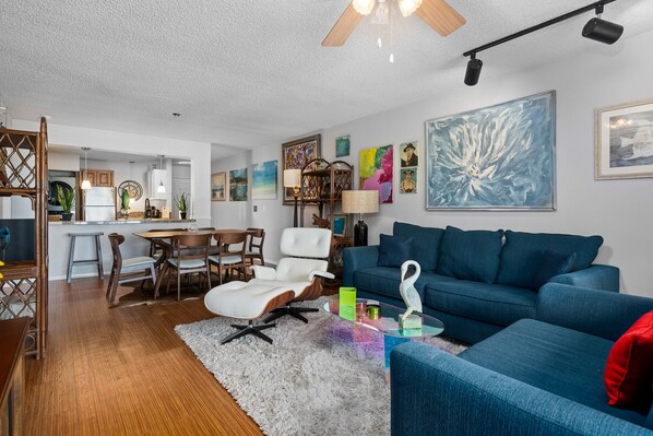 Una sala de estar moderna con un sofá azul, una silla blanca y un comedor con muebles de madera.