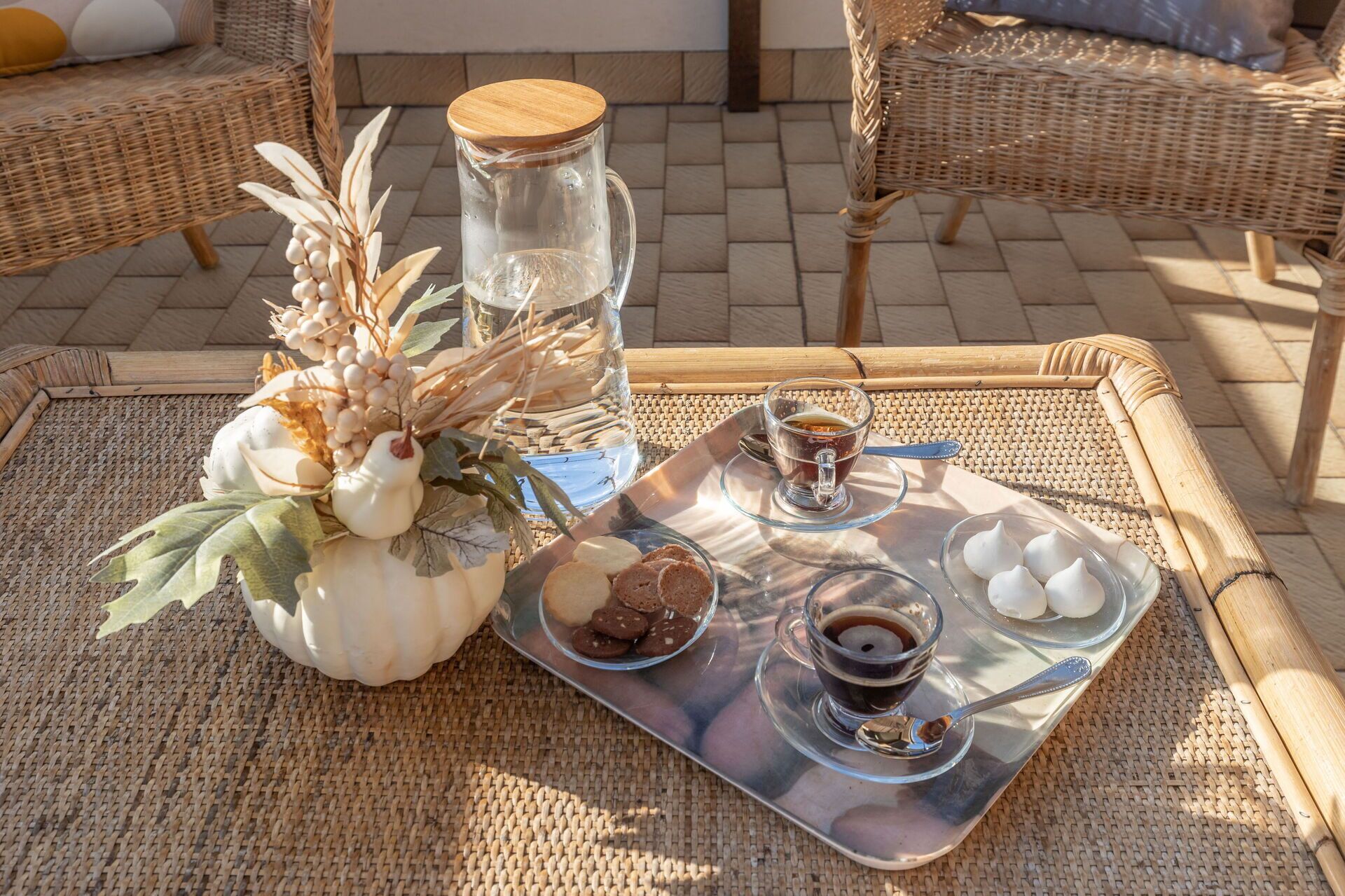 Una mesa de mimbre con una bandeja que contiene galletas, una taza de café y una taza de té, acompañada de elementos decorativos.