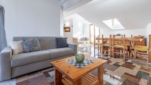 Un vaste espace de vie comprenant un canapé gris, une table basse en bois et un ensemble de salle à manger.