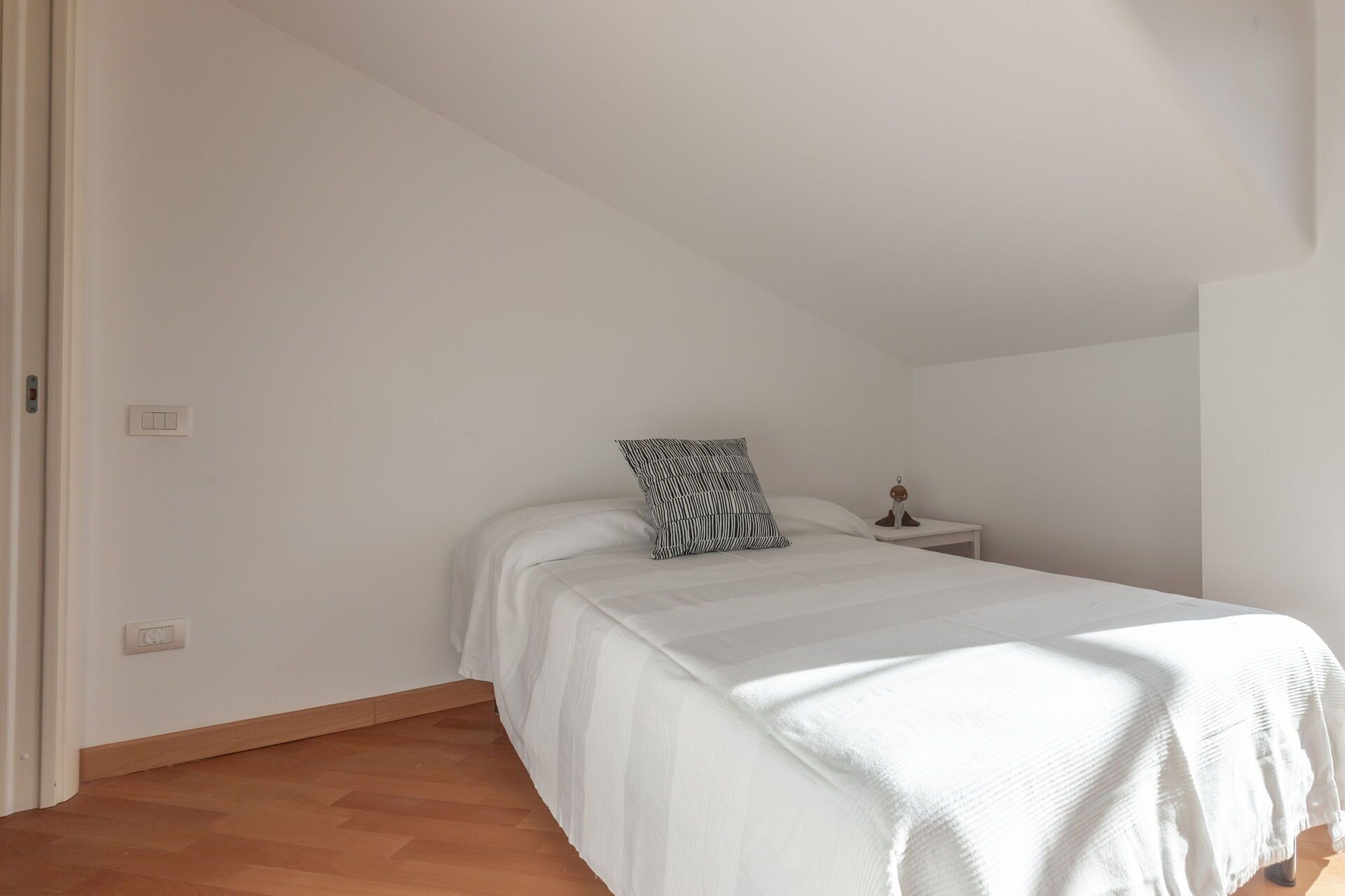 Un dormitorio con una cama, una mesita de noche, una lámpara y una ventana.