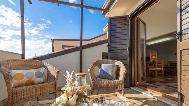 Un balcon avec des fauteuils en osier, un plateau avec des collations et des boissons, et une vue sur l’intérieur.